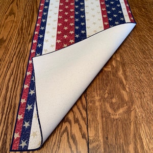May include: A red, white, and blue table runner with a star pattern. The runner is folded over to show the white backing.