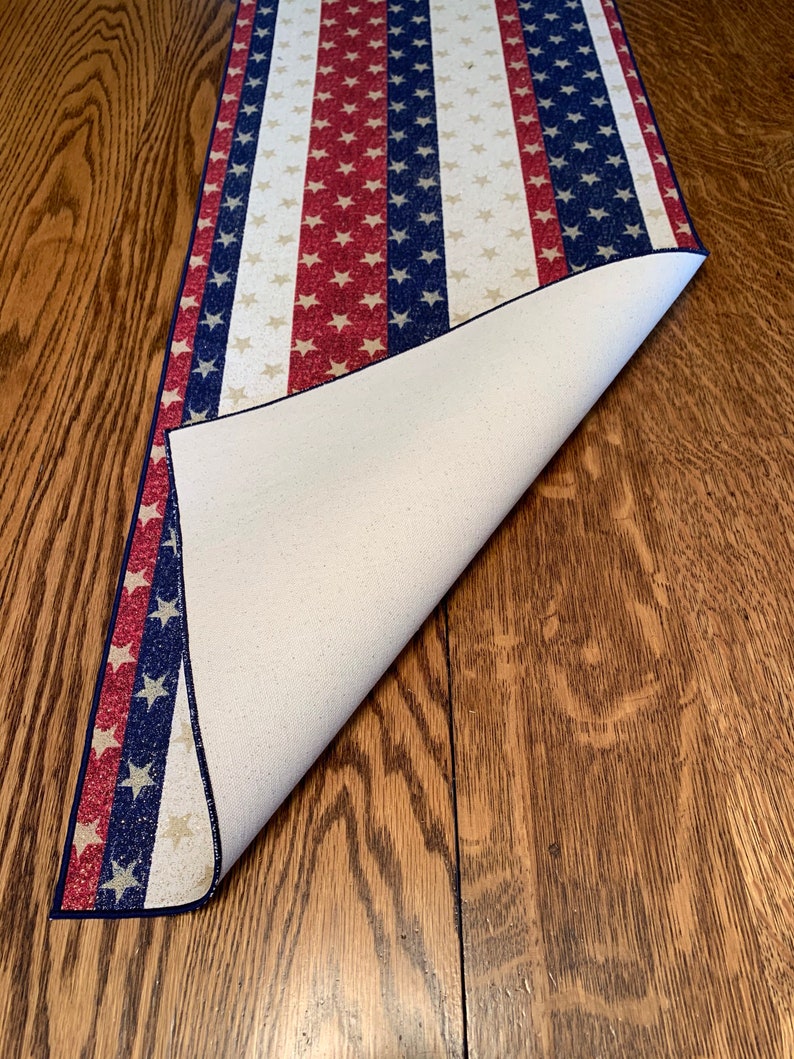May include: A red, white, and blue table runner with a star pattern. The runner is folded over to show the white backing.