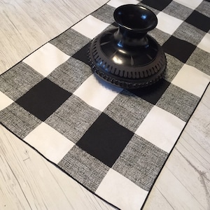 May include: Black and white checkered table runner with a black ceramic vase in the center.