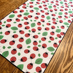 May include: White table runner with a repeating pattern of red ladybugs and green leaves.