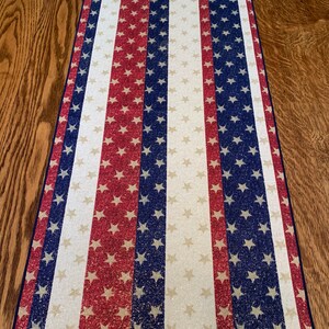 May include: A white table runner with red and blue stripes and white stars. The stripes and stars are a glittery fabric.