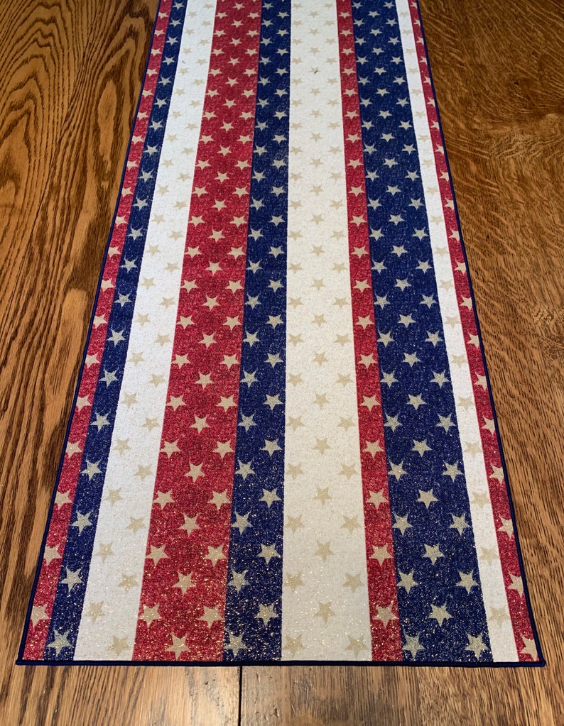 May include: A white table runner with red and blue stripes and white stars. The stripes and stars are a glittery fabric.