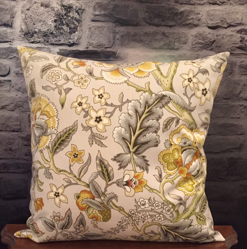 Puede incluir: Una almohada decorativa con un patr&oacute;n floral en tonos amarillos, verdes y grises. La almohada presenta un fondo blanco con un patr&oacute;n repetitivo de flores y hojas estilizadas.