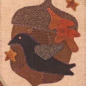May include: A brown and black felt applique pattern for a crow on an acorn. The pattern is 13 inches by 11.5 inches and includes the text "CROW ON ACORN w/rug punch".