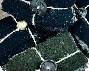 May include: A stack of fabric squares wrapped with twine and secured with black buttons. The fabric is a dark blue and a dark green.