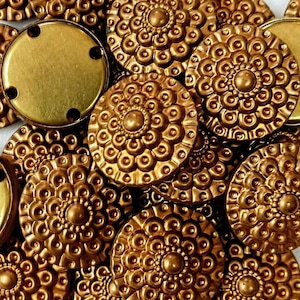 May include: A collection of gold-toned metal buttons with a decorative, raised, circular pattern. The buttons are arranged in a random pattern.