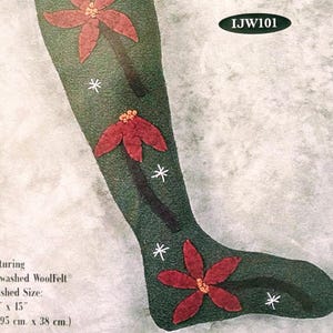 May include: A green Christmas stocking with red flower appliqués and candy canes. The stocking is decorated with white snowflakes and the text "Seems Like Christmas". Finished size is 5.5" x 15".