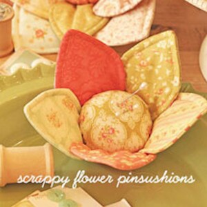 May include: A collection of handmade scrappy flower pincushions in a variety of floral patterns and colors, including red, yellow, and peach. The image also shows buttons and spools of thread. The text "Cherry Blossoms" and "scrappy flower pinsushions" are visible.