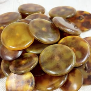 May include: A pile of vintage buttons with a tortoiseshell pattern. The buttons are round and vary in shades of brown and amber. Some buttons have two holes for sewing.