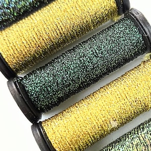 May include: Six spools of metallic thread in shades of gold, green, and iridescent blue. Each spool has a black base and is tightly wound with shimmering thread, ideal for embroidery or crafting projects.