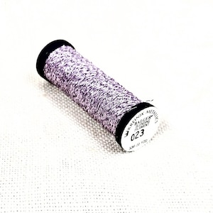 May include: A spool of purple and silver metallic embroidery thread with the text "Kreinik Metallic Braid 023" on the label.