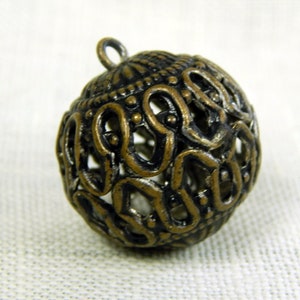 May include: A gold-toned metal ornament with a round, openwork design. The ornament has a loop at the top for hanging.