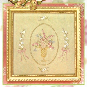 May include: A framed embroidery pattern featuring a bouquet of flowers in a vase, surrounded by sprigs of white pearl buttons. The pattern is titled "Heirloom Button Bouquet" and is for a 9" x 9" stitchery.