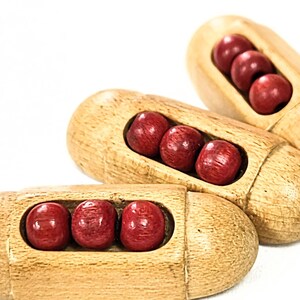 May include: Three wooden puzzle toys, each with a light brown finish and containing three red spheres. The toys are arranged at different angles against a white background, showcasing their design and color contrast.