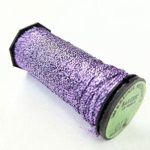 May include: A spool of metallic thread in shades of purple. The thread is tightly wound around a black plastic spool with a green label. The label has text that is partially visible. Ideal for crafting and embroidery projects.