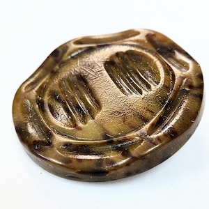 May include: A brown, oval-shaped button with a textured surface and a design featuring two sets of parallel lines. The button has a mottled appearance with darker brown spots and a glossy finish. The button is likely made of a durable material.
