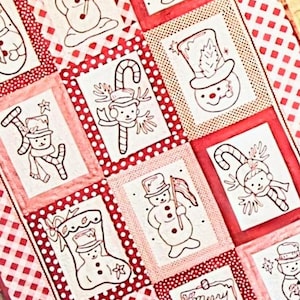 May include: A Christmas-themed quilt featuring a patchwork design with red and white squares. Each square contains a black and white illustration of a snowman, candy cane, or stocking. The quilt has a red and white checkered border.