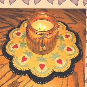 May include: A yellow and green felt pineapple design rug with a black border and a brown glass candle jar in the center.