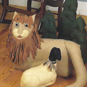 May include: A felt lion, lamb, and trees pattern. The lion is tan with a brown mane, the lamb is cream-colored, and the trees are dark green. The text "PEACE TO ALL" is at the top.