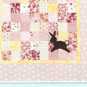 May include: Patchwork Rabbit quilt pattern, a quick and easy baby quilt project. The pattern features a patchwork design with pink, yellow, and white fabrics. The quilt is 38 inches by 50 inches.