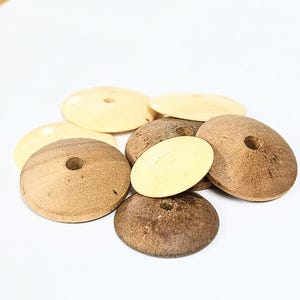 May include: A collection of circular, disc-shaped buttons featuring a central hole. The buttons are crafted from wood and display two distinct finishes: a smooth, light cream-colored surface and a textured, darker brown wood grain finish.