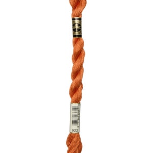 May include: A skein of DMC embroidery floss in color 922, a bright orange. The floss is wrapped around a white label with black text and a barcode.