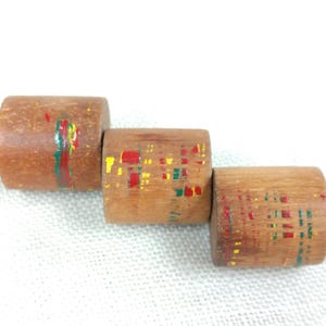 May include: Three wooden cylinders with colorful geometric patterns painted on them. The cylinders are stacked on top of each other.