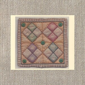 May include: A small, square quilt with a patchwork design of diamond shapes in shades of pink, green, blue, and purple. The quilt is edged with a brown trim and has five green buttons sewn on.