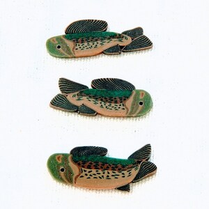 May include: Three ceramic fish ornaments with brown, green, and black paint. The fish are all facing the right side of the image.