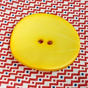 May include: A large, round, yellow button with two holes. The button is made of a smooth, shiny material.