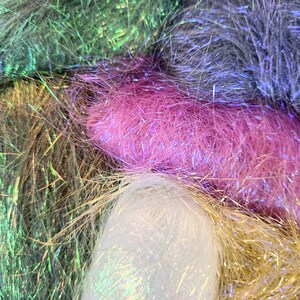 May include: Close-up of a collection of colorful, iridescent tinsel strands. The tinsel is in shades of pink, green, gold, silver, and purple. The strands are soft and fluffy, with a metallic sheen.