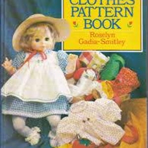 May include: A vintage book titled "Dolls' Clothes Pattern Book" with a doll wearing a dress and hat. The cover is yellow with the title in green and the author's name. Various doll clothes are scattered around the doll.