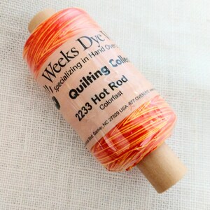 May include: A spool of Weeks Dye Works quilting thread in the color "2233 Hot Rod". The thread is a blend of orange and red and is colorfast. The spool is labeled with the company name, the thread color, and the colorfast information.