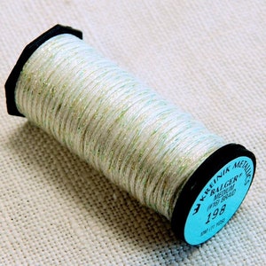 May include: A spool of white thread with a metallic sheen and green accents. The spool is labeled "Kreinik Metallics Balger Medium 1/16" 198"