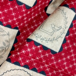 May include: Red fabric with a white star pattern and a beige fabric with a black outline and a bird design. The fabric is folded in half.