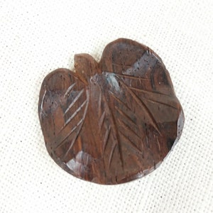May include: A dark brown wooden carving of a leaf with intricate details. The carving is smooth and polished, with a natural wood grain.