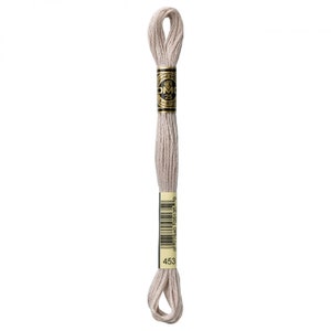 May include: A skein of DMC embroidery floss in color 453, a light beige. The floss is wrapped around a cardboard spool with a black and gold label that reads "DMC" and "25m (8.2 yd) 6-Strands."