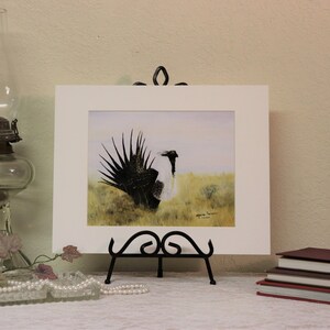 May include: A framed watercolor painting of a black and white bird with a long tail, standing in a field of grass. The painting is signed by the artist, "Mark Swanson".