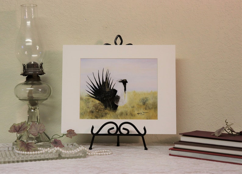 May include: A framed watercolor painting of a black and white bird with a long tail, standing in a field of grass. The painting is signed by the artist, "Mark Swanson".
