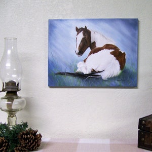 May include: A painting of a brown and white horse lying down on a blue background. The horse is looking to the left. The painting is signed by the artist.