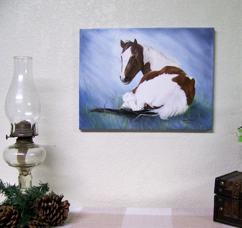 May include: A painting of a brown and white horse lying down on a blue background. The horse is looking to the left. The painting is signed by the artist.