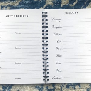 May include: A white spiral bound notebook with the words "Gift Registry" and "Vendors" printed on the front and back covers. The notebook has sections for listing store information, including store name, address, website, notes, login, and password. The back cover has sections for listing vendor information, including ceremony, reception, catering, cake, florist, photos, videos, music, and coordinator.