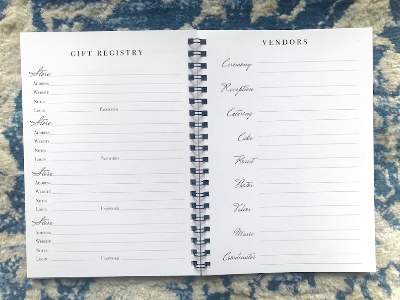 May include: A white spiral bound notebook with the words "Gift Registry" and "Vendors" printed on the front and back covers. The notebook has sections for listing store information, including store name, address, website, notes, login, and password. The back cover has sections for listing vendor information, including ceremony, reception, catering, cake, florist, photos, videos, music, and coordinator.