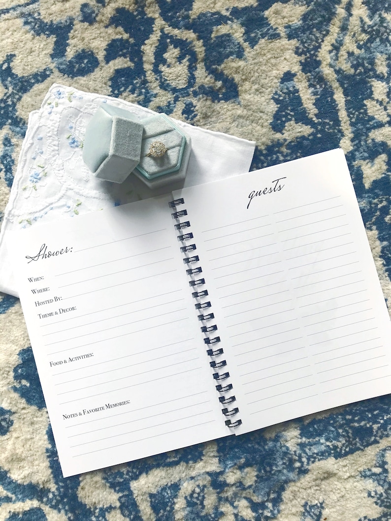 May include: A white notebook with a blue spiral binding. The notebook has lined pages and the words "Shower:" and "Guests" written on the front and back covers.
