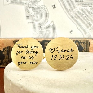 May include: A pair of gold cufflinks with engraved messages. One cufflink says "Thank you for loving me as your own". The other cufflink says "Sarah 12.31.24" with a heart symbol.