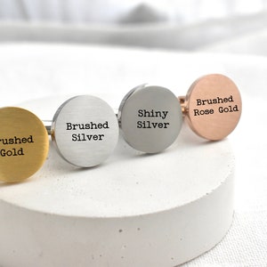 May include: Four cufflinks in different finishes: brushed gold, brushed silver, shiny silver, and brushed rose gold. Each cufflink has the finish and metal type engraved on the face.