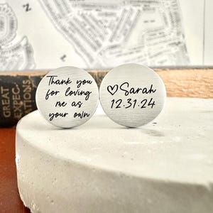 May include: Two silver cufflinks with engraved messages. The first cufflink says "Thank you for loving me as your own". The second cufflink says "Sarah 12.31.24" with a heart symbol.
