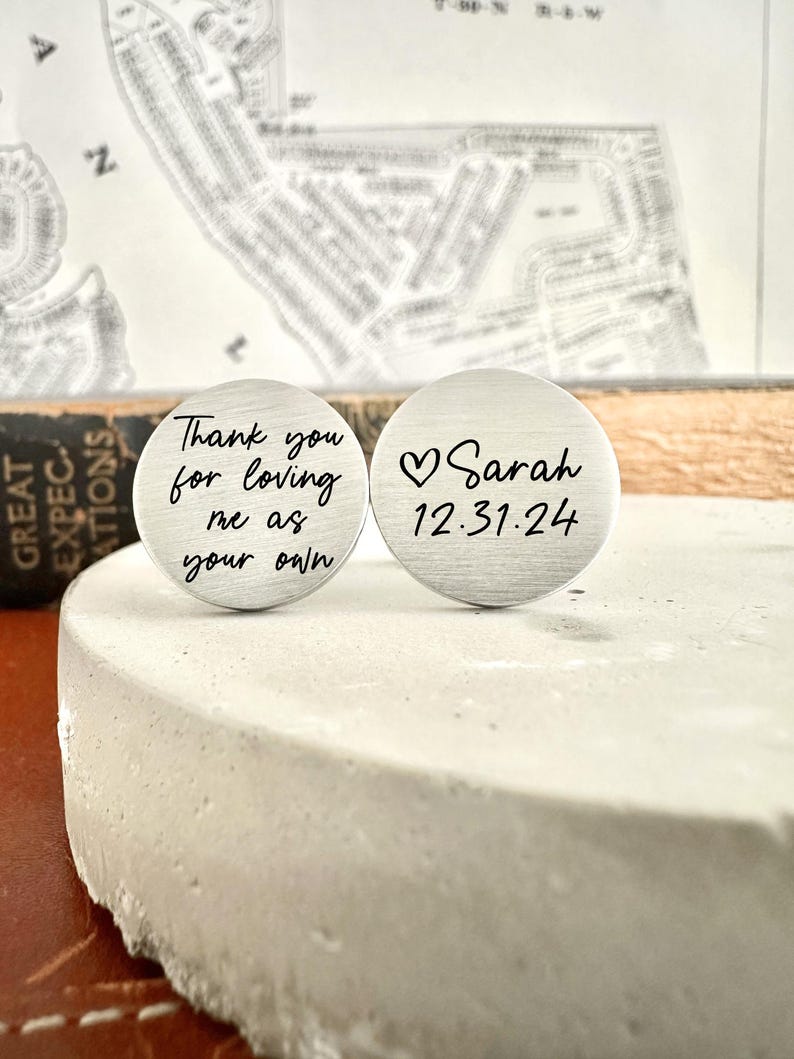 May include: Two silver cufflinks with engraved messages. The first cufflink says "Thank you for loving me as your own". The second cufflink says "Sarah 12.31.24" with a heart symbol.