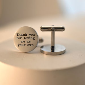 May include: Silver cufflinks with a round, engraved message that reads "Thank you for loving me as your own".