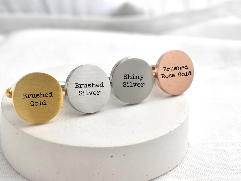 May include: Four cufflinks in different finishes: brushed gold, brushed silver, shiny silver, and brushed rose gold. Each cufflink has the finish and metal type engraved on the face.